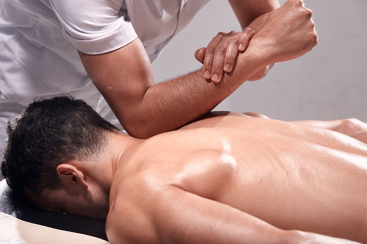 massage therapist performing deep tissue massage on a man lying down facing down